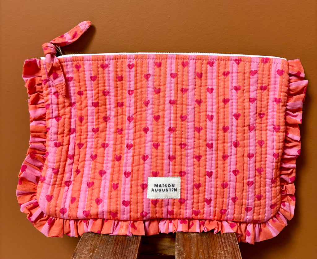 Grande pochette cœur rose et rouge à volant maison Augustin Devant un mur terracota et posé sur un tabouret 
