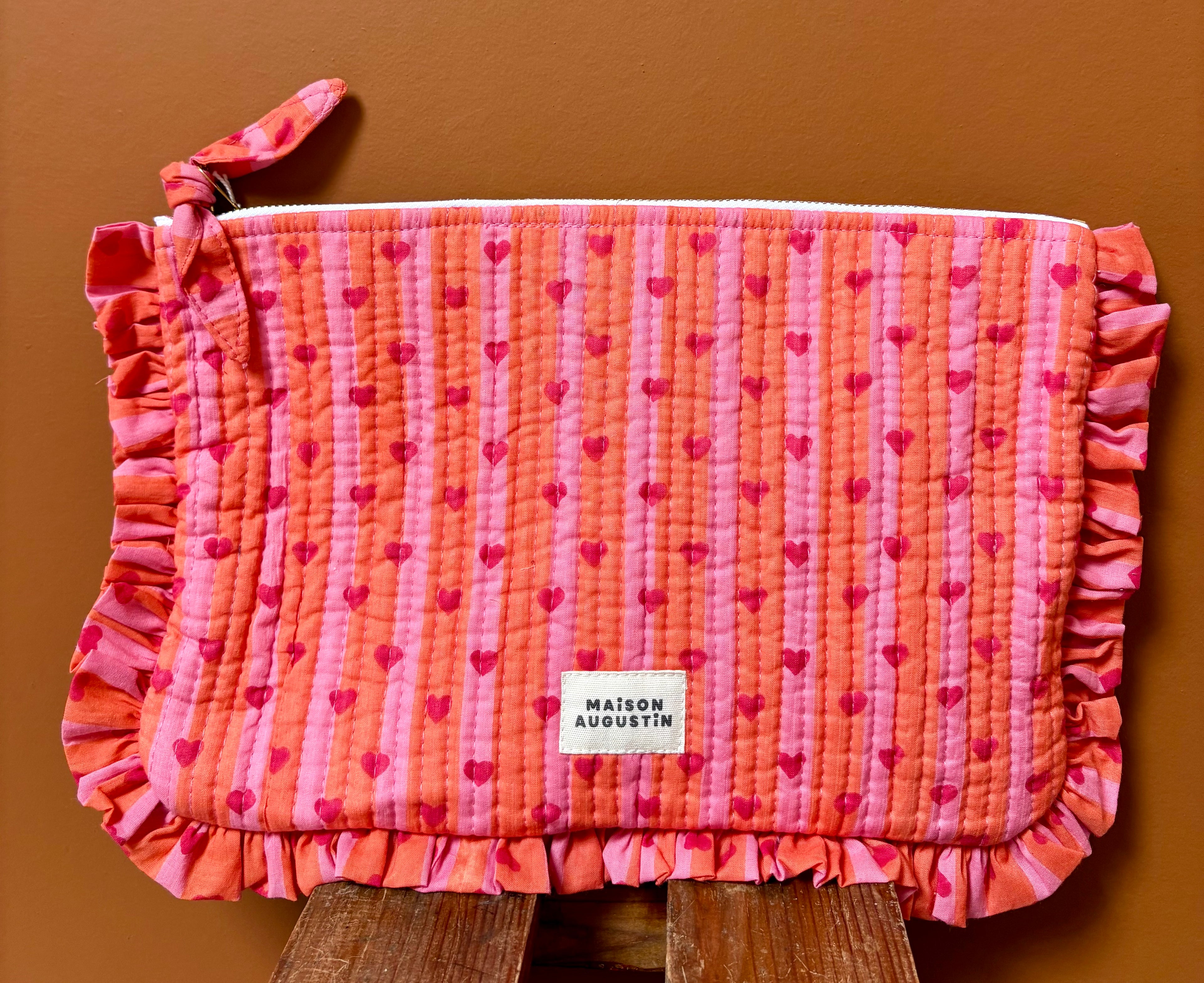 Grande pochette cœur rose et rouge à volant maison Augustin Devant un mur terracota et posé sur un tabouret 